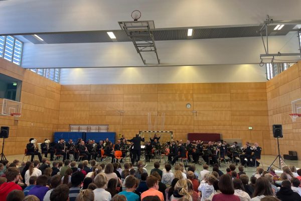 Schüler sitzen in der Turnhalle und lauschen dem Konzert des Polizeiorchesters